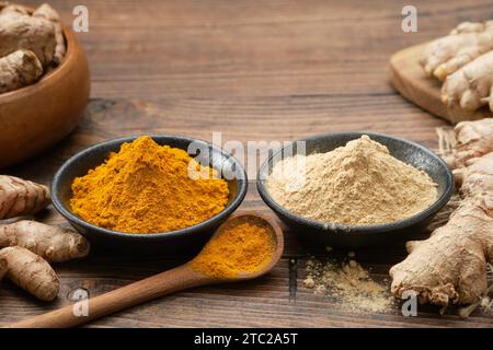 Bowls of ginger and curcuma ground to powder and whole ginger and turmeric roots on kitchen table. Aromatic spices. Stock Photo