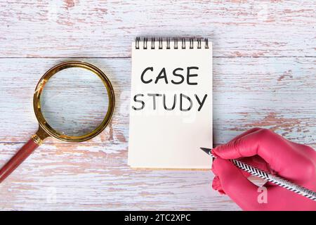 Case study I am writing on a notebook lying on old boards next to a magnifying glass and a hand in a red medical glove with a pencil Stock Photo