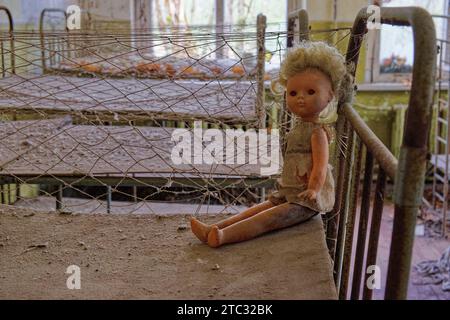 An old doll sitting on a ledge in an abandoned room. A dirty doll on a rusty baby bed. Abandoned bedroom in kindergarten. Chernobyl radioactive zone. Stock Photo