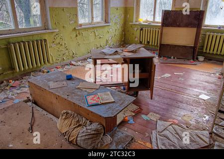 The image shows an abandoned room with a desk, a bookshelf, and a radiator. The walls are peeling and the floor is covered in debris. An abandoned kin Stock Photo