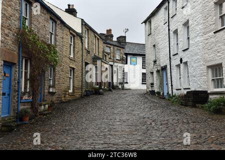 The cobbled main street through Dent village in Dentdale  - in the distance is the Sun Inn with cobbled streets and old houses in the centre Stock Photo