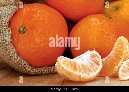 close up of fresh tangerines in jute bag with peeled pieces on wooden table Stock Photo