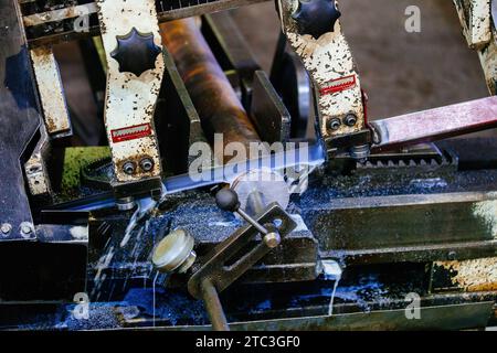 Automatic band saw machine with the liquid coolant is cutting metal rod, close up. Stock Photo