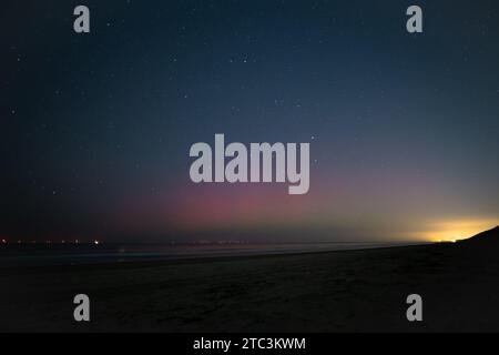 Purple colored northern lights or aurora borealis under a starry sky on the North Sea beach. Stock Photo