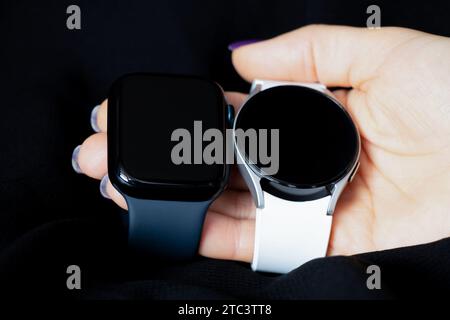 Dnipro, Ukraine - December 10, 2023: White smart watches Samsung Galaxy Active and Apple Watch Series 8 are held by a female hand, two smart watches t Stock Photo