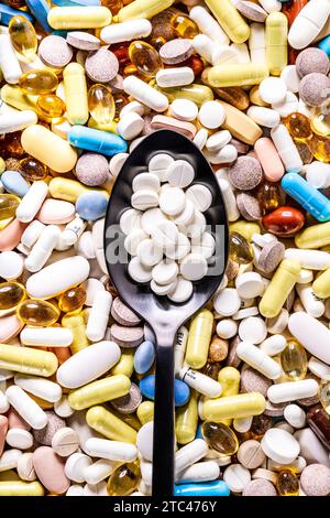 Round pills on a spoon with pills, tablets and capsules in background Stock Photo