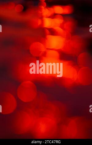 Red out of focus specular highlights created by a setting sun reflecting off moving water Stock Photo