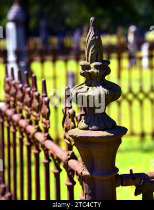 Rustic iron fence surrounds graves at a cemetery.  It is rusting but decorative and fancy. Stock Photo