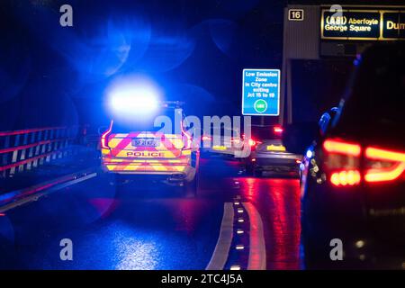 Police car with blue flashing lights at night responding to an emergency and joining heavy traffic on M8 motorway via junction 15 Glasgow Scotland, UK Stock Photo