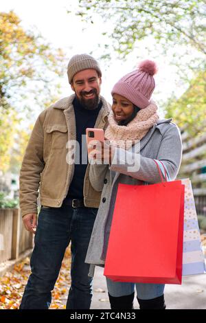 Young interracial couple using phone while walking in the street doing christmas shopping together. Stock Photo