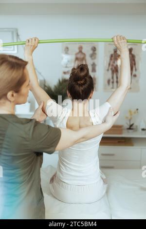 Healthcare time. Seen from behind female medical massage therapist in massage cabinet with client doing checkup. Stock Photo