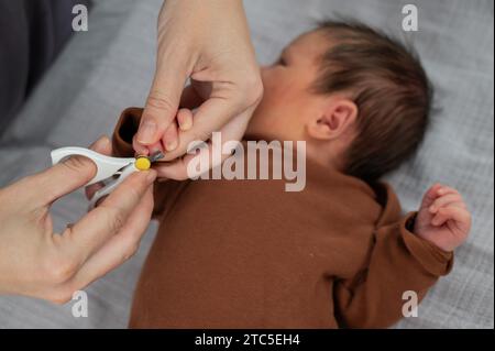 Mom cuts her newborn son's fingernails with small children's scissors. Stock Photo