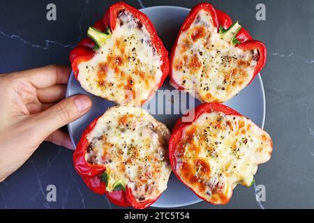 Hand Placing a Plate of Delectable Homemade Stuffed Bell Peppers on Black Marble Table Stock Photo