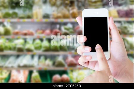 Woman using mobile phone while shopping in supermarket, grocery store Stock Photo