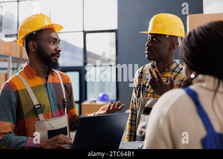 Storehouse managers checking delivery online invoice on laptop and talking. African american logistics managers discussing stock supply chain in cargo distribution department warehouse Stock Photo