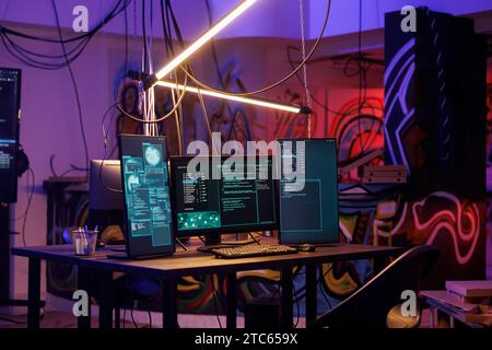 Computers with malicious ransomware running code on screens in abandoned warehouse. Encryption software multiple windows and password hacking activity on monitors in dark room Stock Photo