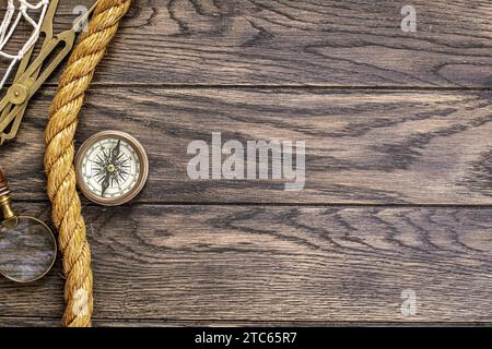 Adventure travel concept. Vintage compass, magnifying glass and hawser rope on old wooden table background with copy space Stock Photo
