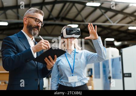 Engineers talking project using VR, in modern industrial factory. Virtual reality in manufacturing industry, Smart glasses guiding female and male Stock Photo
