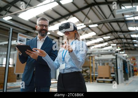 Engineers talking project using VR, in modern industrial factory. Virtual reality in manufacturing industry, Smart glasses guiding female and male Stock Photo