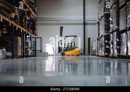 Side view of forklift in warehouse with male driver. Warehouse worker preparing products for shipmennt, delivery, checking stock in warehouse. Stock Photo