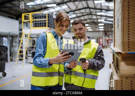 Young man with Down syndrome working in warehouse, female colleague teaching him scan products with scanner. Concept of workers with disabilities Stock Photo