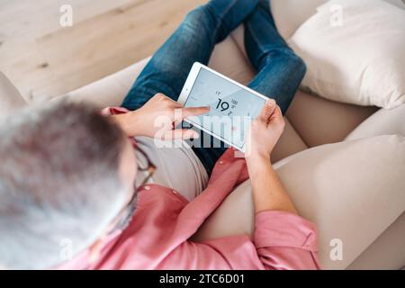 Man using smart thermostat, adjusting, lowering heating temperature at home. Concept of sustainable, efficient, and smart technology in home heating Stock Photo