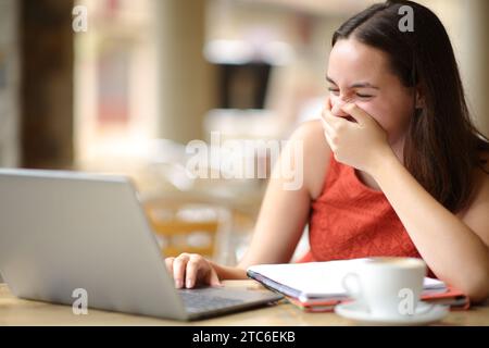 Happy student laughing loud watching media on laptop in a coffee shop terrace Stock Photo