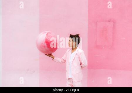 Young boy all pink holding a ball on the sidewalk in a suit Stock Photo
