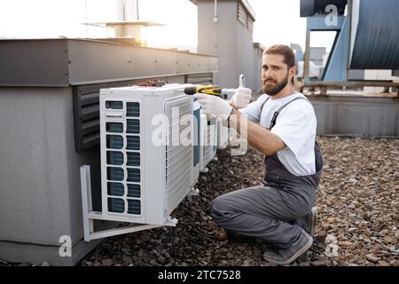 Male worker repairing conditioner while using drill outdoor Stock Photo
