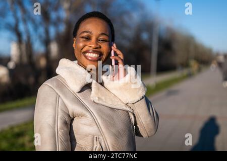 Outdoor portrait of happy black woman. She is talking on phone. Stock Photo