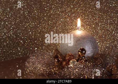 Close-up of a silver burning ball candle on a Christmas decorated plate against glittering background, copy space on the left side, side view Stock Photo