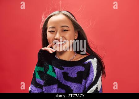 happy young asian woman in knitted sweater with animal print posing on red background Stock Photo