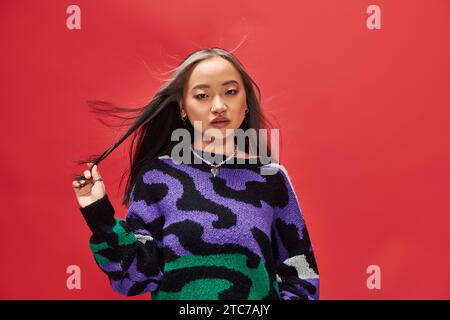 beautiful young asian woman in vibrant sweater with animal print with heart shaped necklace on red Stock Photo