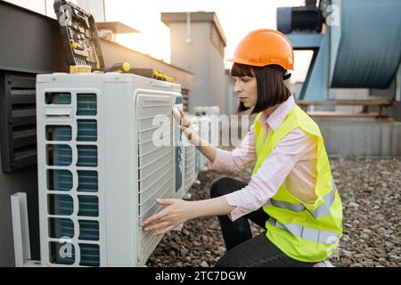 Beautiful brunette in helmet inspecting air conditioner Stock Photo