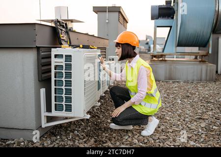 Beautiful brunette in helmet inspecting air conditioner Stock Photo