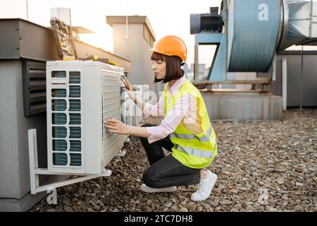 Beautiful brunette in helmet inspecting air conditioner Stock Photo