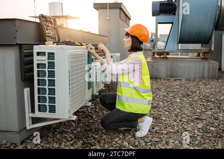 Woman using screwdriver for fixing air conditioner on roof Stock Photo