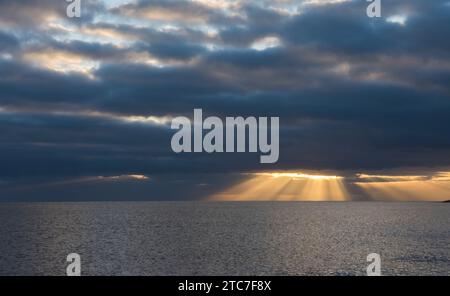 sunbeams shining through gap in dark, black clouds onto the horizon of the sea. winter, November, Devon, UK Stock Photo