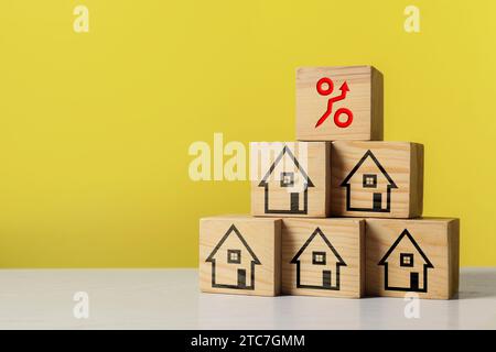 Mortgage rate rising illustrated by percent sign with upward arrow. Pyramid of wooden cubes with house icons on table, space for text Stock Photo