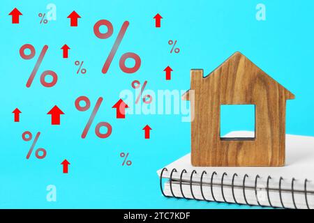 Mortgage rate rising illustrated by upward arrows and percent signs. House model and notebook on light blue background Stock Photo