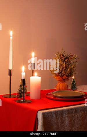 christmas table, candles, flowers, red tablecloth and plates, dim yellow light Stock Photo
