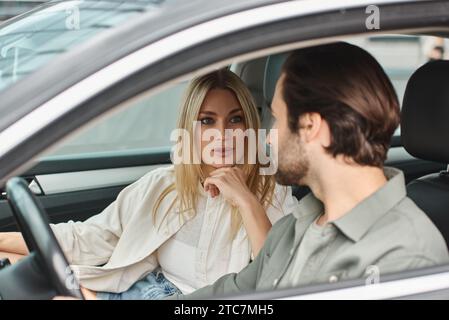 attractive blonde woman looking at handsome bearded man while sitting in modern car, seduction Stock Photo
