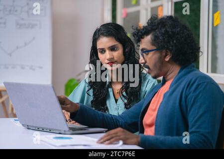young man explaining project or problem details to female colleague from laptop at office - concept of team cooperation, client business meeting and Stock Photo