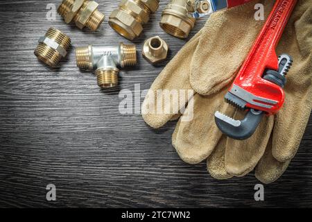 Plumbing monkey wrench pipe fittings protective gloves water valve on wooden board Stock Photo