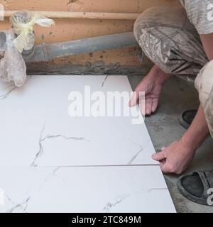 A male builder tiler lays floor ceramic tiles. Selective soft focus Stock Photo