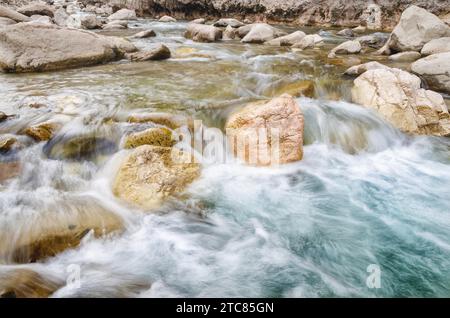 A river of fresh water among the rocks. Fresh aqua fast flow in the stones. A forest river with clean cold water. Fresh spring in the mountains. Stock Photo