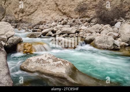 A river of fresh water among the rocks. Fresh aqua fast flow in the stones. A forest river with clean cold water. Fresh spring in the mountains. Stock Photo