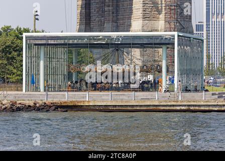 Jane’s Carousel stands in the shadow of the Brooklyn Bridge. The glass-enclosed children’s amusement was moved from Youngstown, Ohio. Stock Photo