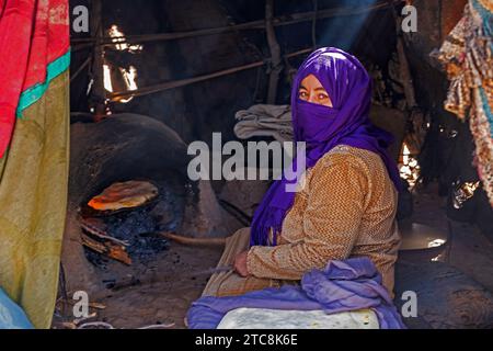 Nomadic Bedouin woman with hijab baking bread in traditional oven in tent in the Sahara Desert near Merzouga, Drâa-Tafilalet, Errachidia, Morocco Stock Photo