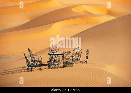 Cast iron garden table and lawn chairs in sand dunes of Erg Chebbi in the Sahara Desert near Merzouga, Drâa-Tafilalet, Errachidia, Morocco Stock Photo